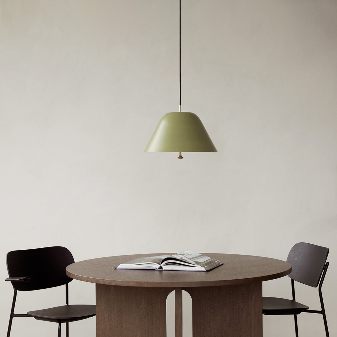 Sleek olive green pendant light hanging over a round wooden table with black and wood accent chairs. Modern minimalist design.