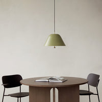 Sleek olive green pendant light hanging over a round wooden table with black and wood accent chairs. Modern minimalist design.