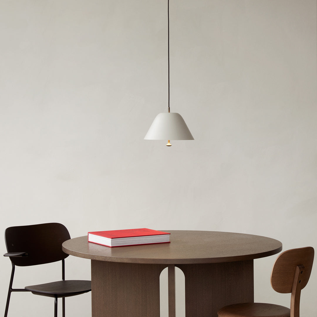 Minimalist white pendant lamp above a round wooden table, complemented by black and brown chairs and a red book.