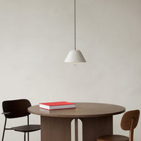 Minimalist white pendant lamp above a round wooden table, complemented by black and brown chairs and a red book.