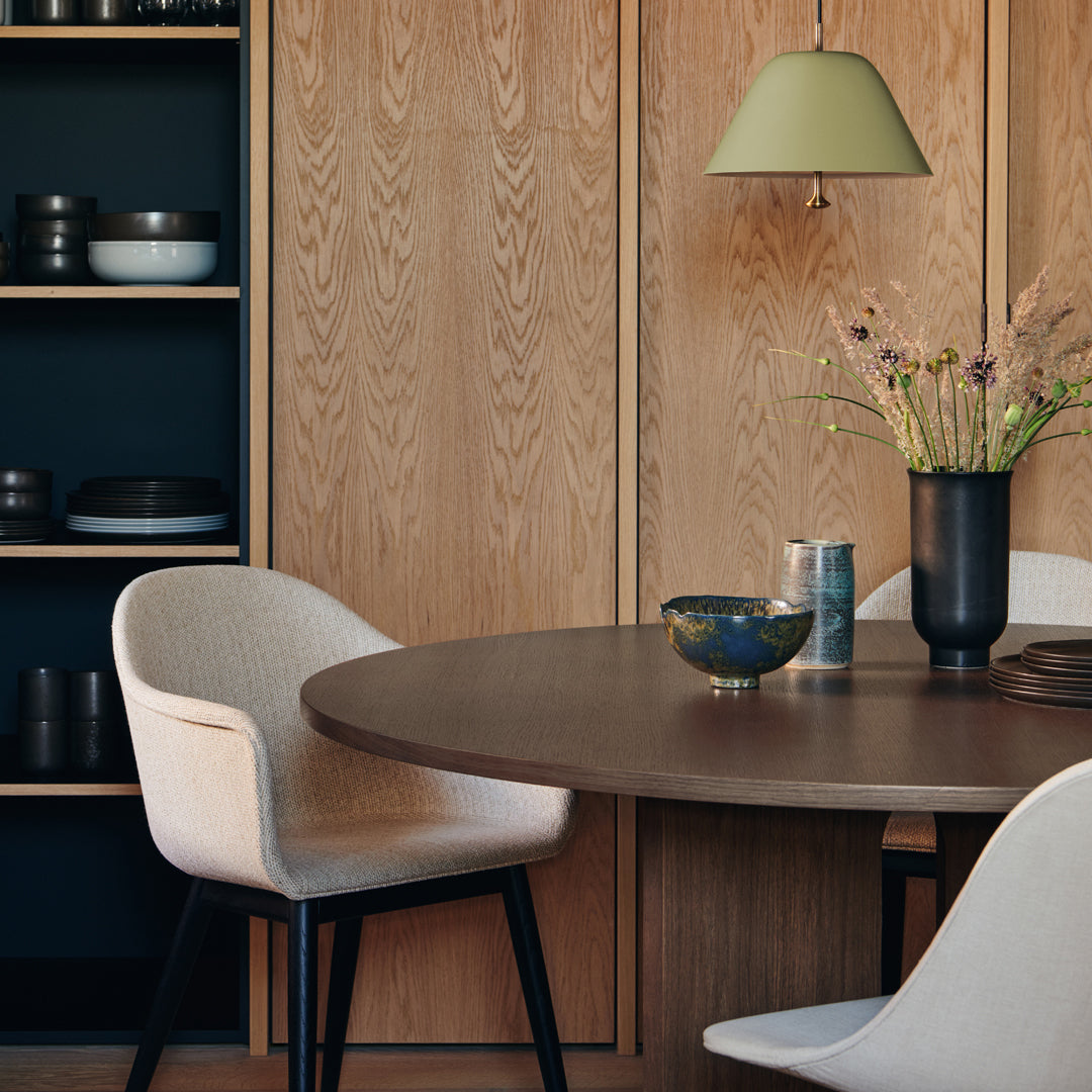 Minimalist dining room featuring a round wooden table, beige chairs, and a green pendant light, with natural wood and dark accents.