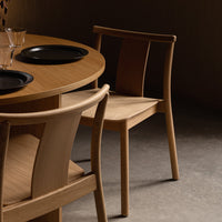 Natural wood finish dining chair with smooth curves, paired with a round wooden table and black plates.