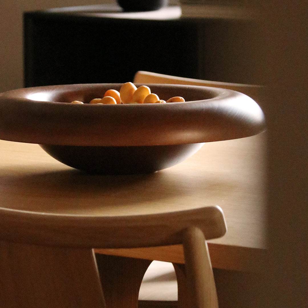 "Wooden bowl with a smooth, dark finish, filled with bright yellow fruits, set on a light wood table."