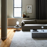 Minimalist living room featuring a neutral-toned sofa, gray marble table, and soft beige rug with natural light.
