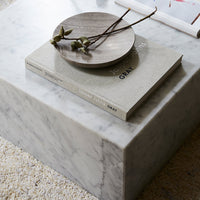 Elegant white marble coffee table with gray accents, featuring a minimalist gray book and a round wood plate.