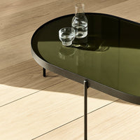 Oval coffee table with a dark green glass top and sleek black metal legs, set against a light wood floor.