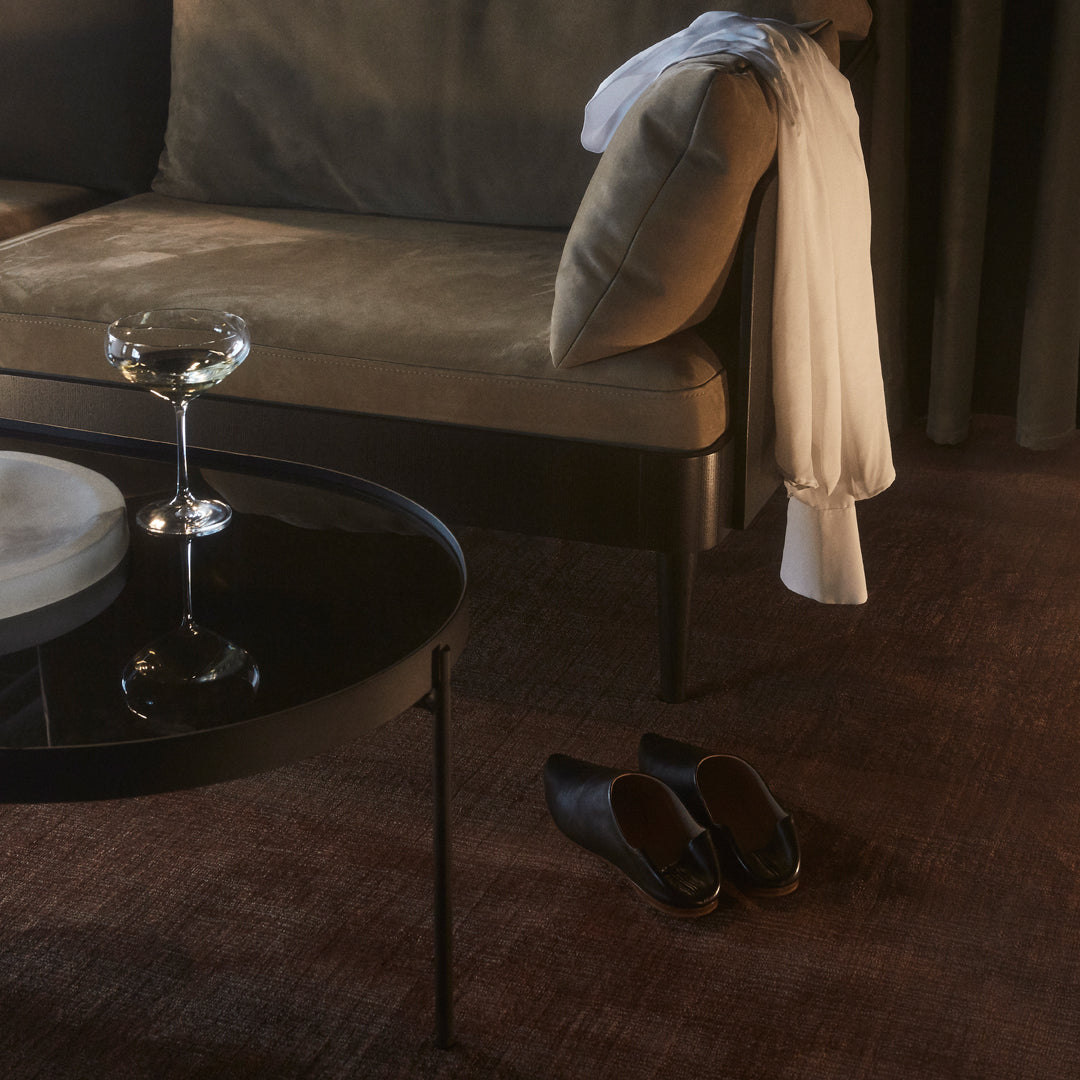 Velvet green and beige sofa with a glossy black table, brown rug, and white fabric adding contrast to the warm tones.