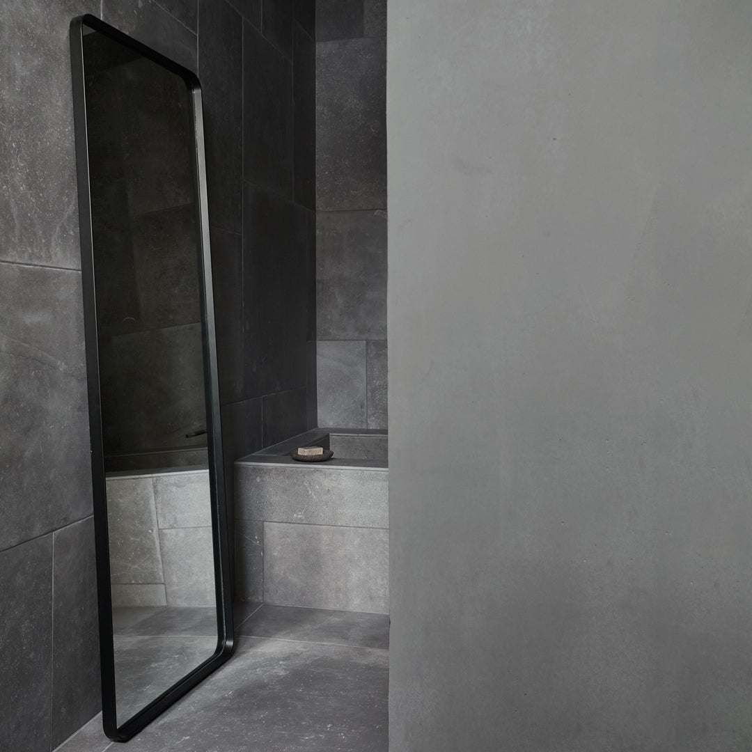 Sleek black rectangular mirror against textured dark gray tiled wall in a modern bathroom setting.