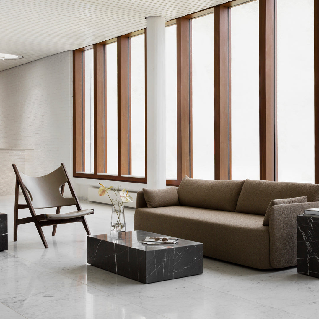 Brown sofa and sleek black marble tables set against modern white walls and wooden window frames with warm tones.
