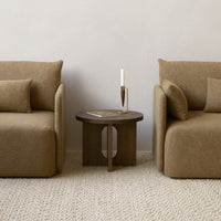 Brown textured armchairs with matching cushions and a dark wood side table on a neutral-toned woven rug.