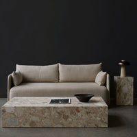 Beige upholstered sofa with textured cushions, paired with a light stone coffee table and modern dark accents.