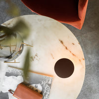 Round marble tabletop in creamy tones with veining, complemented by a sleek black circle, and a warm terracotta chair.