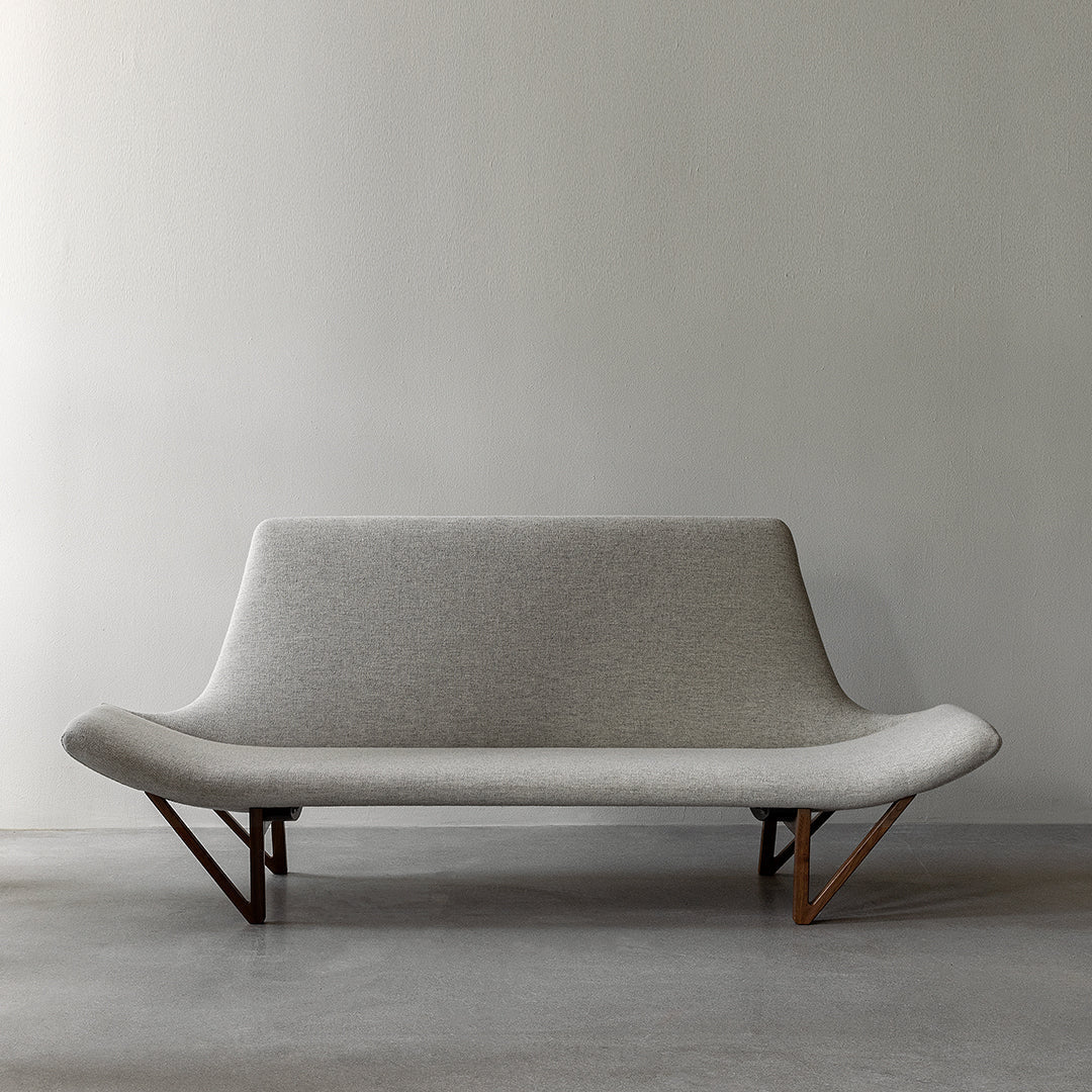 Gray fabric sofa with smooth curves and wooden legs against a minimalistic backdrop.