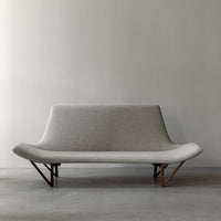 Gray fabric sofa with smooth curves and wooden legs against a minimalistic backdrop.