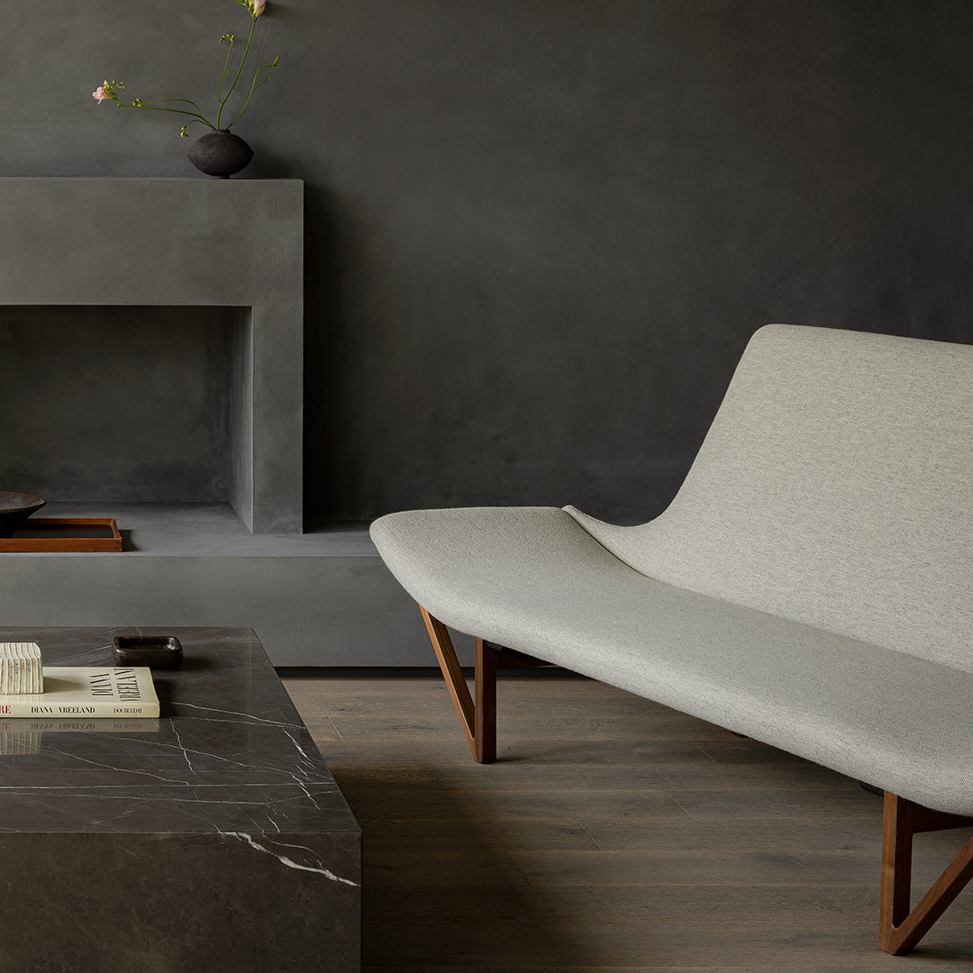 Light gray sofa against a dark textured wall, with a dark marble table and warm wood accents. Elegant modern design.