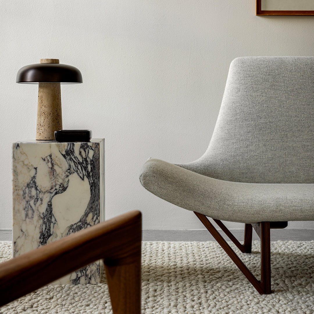 Gray upholstered chair with a marble side table featuring black and white patterns and warm wooden accents.