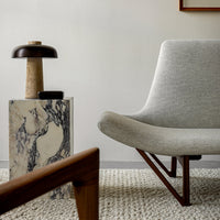 Gray upholstered chair with a marble side table featuring black and white patterns and warm wooden accents.