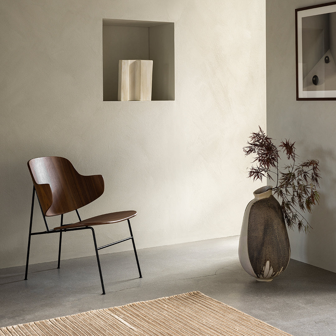 Mid-century wood chair in deep brown against soft beige wall; textured gray floor with woven light tan rug.