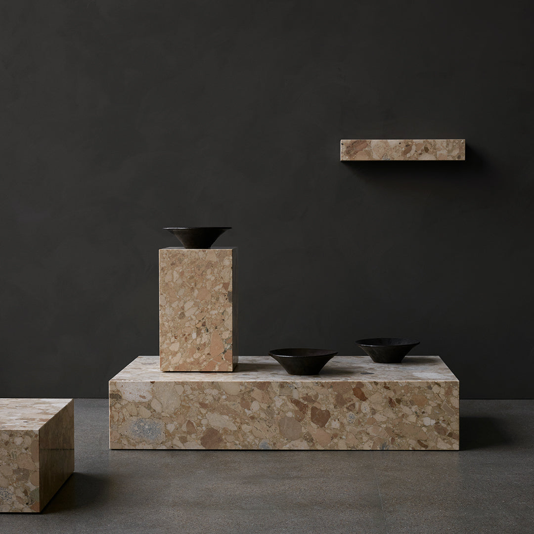 Stylish display of beige terrazzo surfaces with black bowls against a dark backdrop, highlighting texture and contrast.