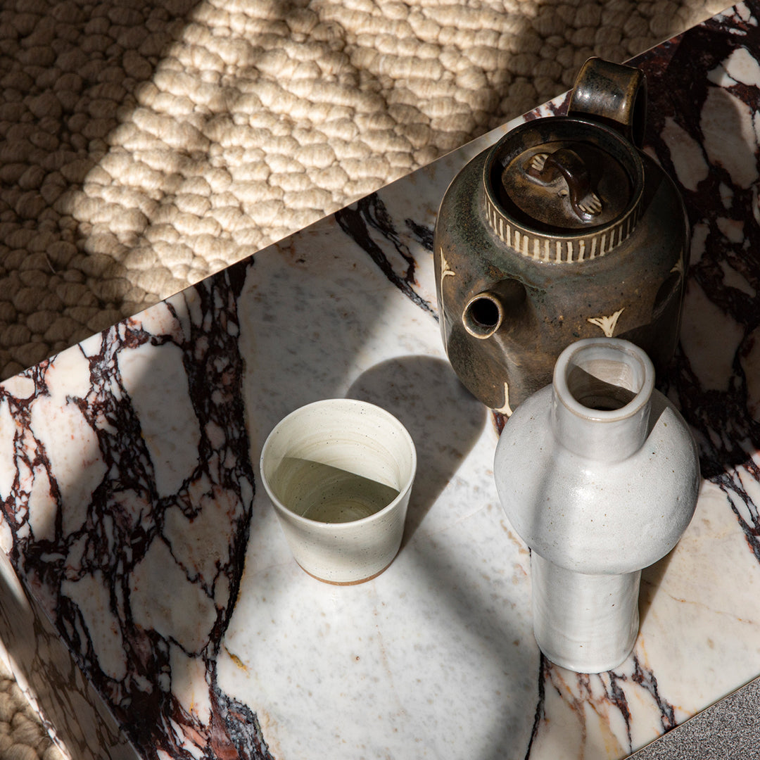 "Elegant marble tray with rich red and white veining, showcasing ceramic vessels in soft hues against a textured backdrop."