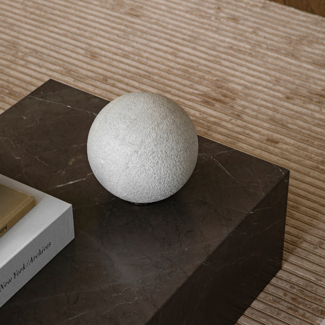 Textured white sphere on a dark stone surface, contrasting with subtle striped background. Elegant modern decor.