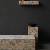 Textured beige stone table with earthy tones and a dark backdrop, featuring a simple black bowl.