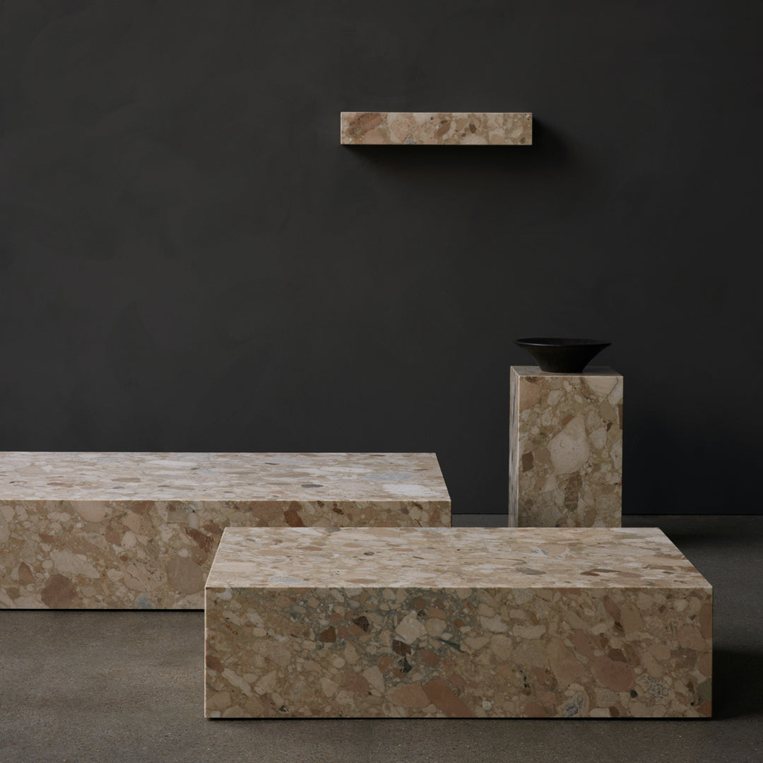Textured beige and pink terrazzo tabletop with gray flecks against a dark wall, featuring minimalist design elements.