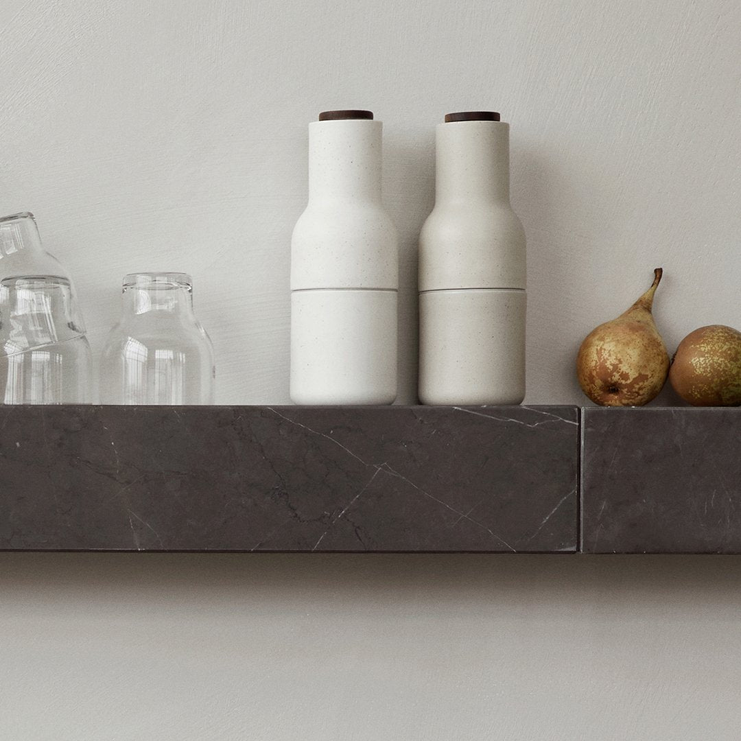 White and light gray ceramic bottles with dark brown lids on a dark marble shelf, complemented by transparent glassware.