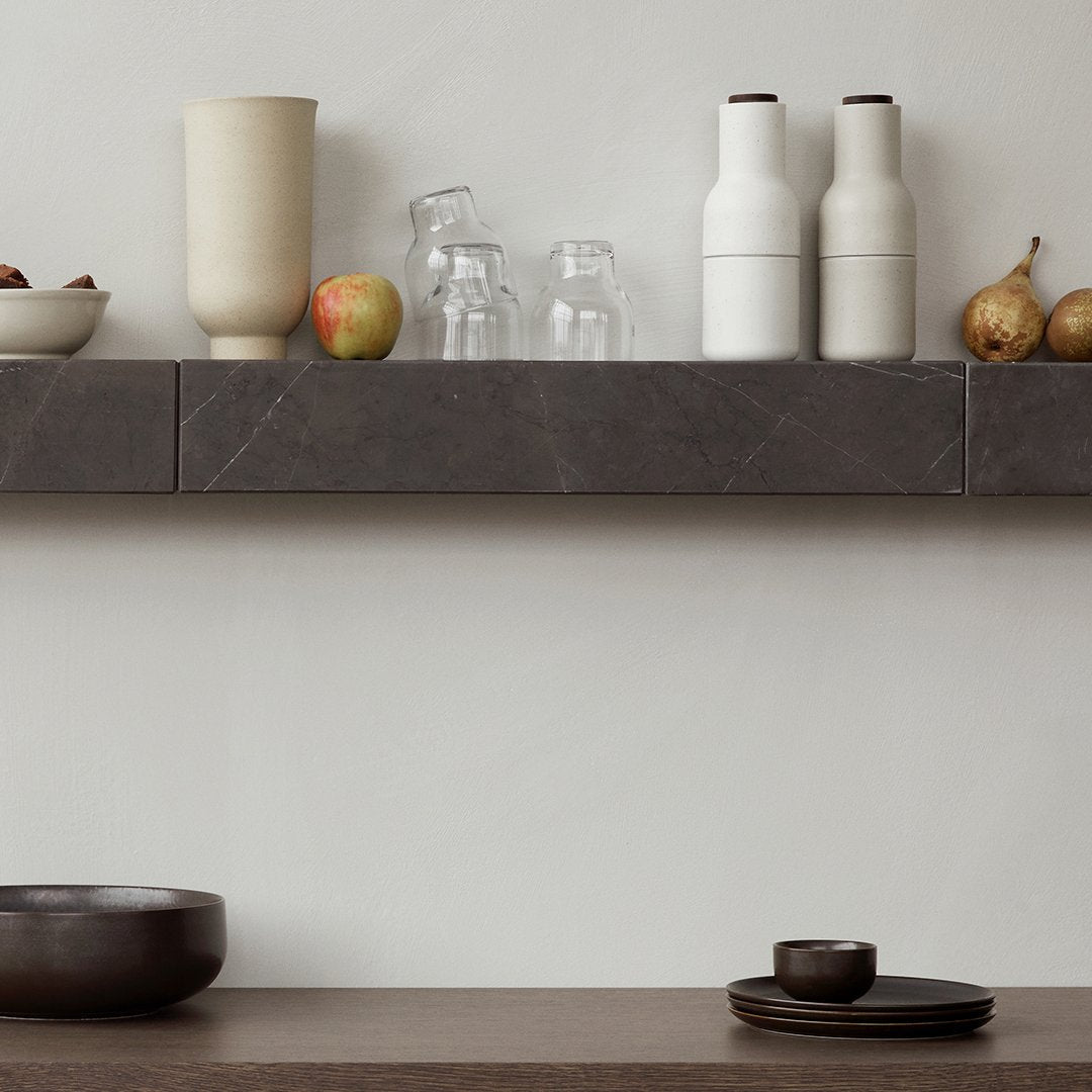 Neutral gray and beige pottery, clear glassware, and dark wooden bowl showcase a minimalist, modern aesthetic.