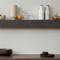 Neutral gray and beige pottery, clear glassware, and dark wooden bowl showcase a minimalist, modern aesthetic.