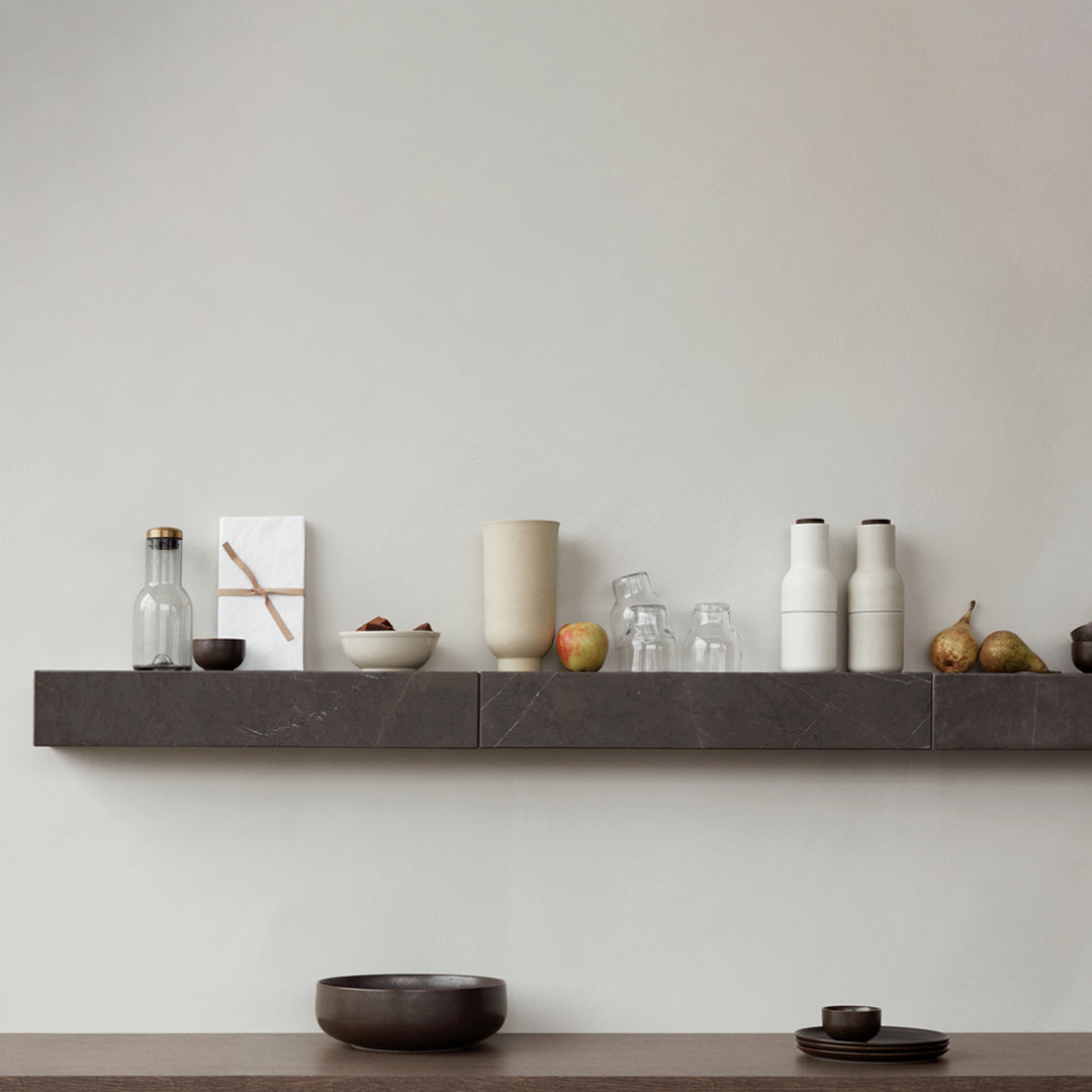 Minimalist shelf display featuring earthy tones, clear glass, and textured ceramics on a sleek dark surface.