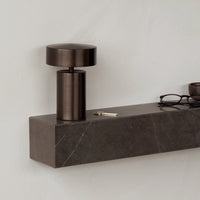 Modern dark bronze lamp on a sleek marble shelf with grey and white veining against a neutral wall.