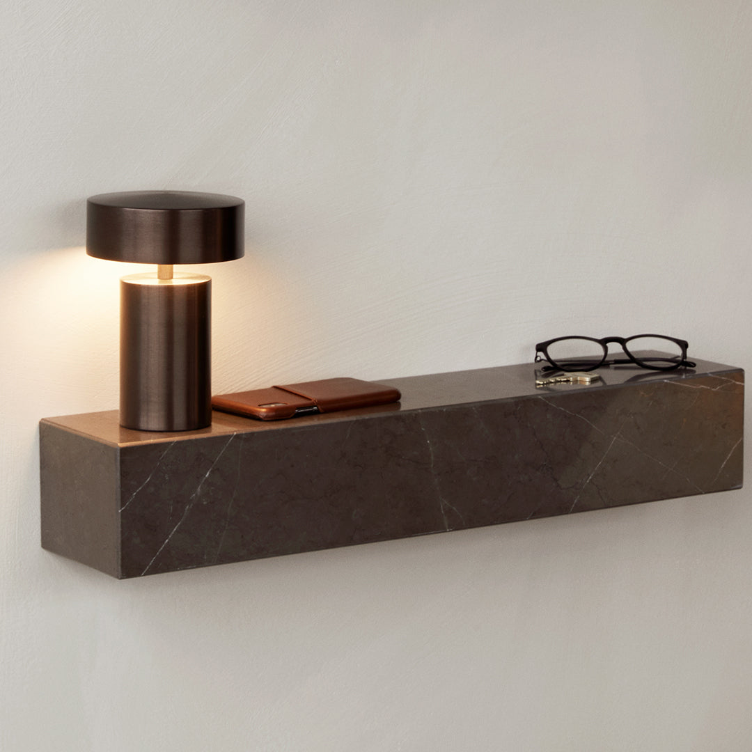 Modern wall shelf with a sleek dark marble pattern and a warm bronze lamp; stylish and minimalist design.