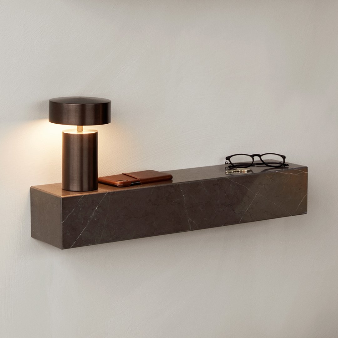 "Stylish brown marble shelf with a modern bronze table lamp, accented by warm light and chic accessories."