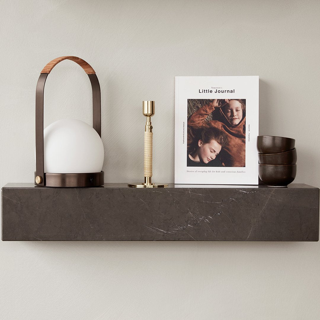 Brown and gold accents with a white spherical lamp, dark marble shelf, and neutral-toned book for a modern aesthetic.