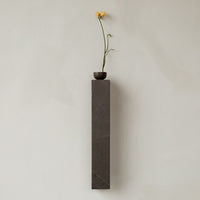 Tall gray marble vase with a dark bowl and a vibrant yellow flower against a soft, light beige background.