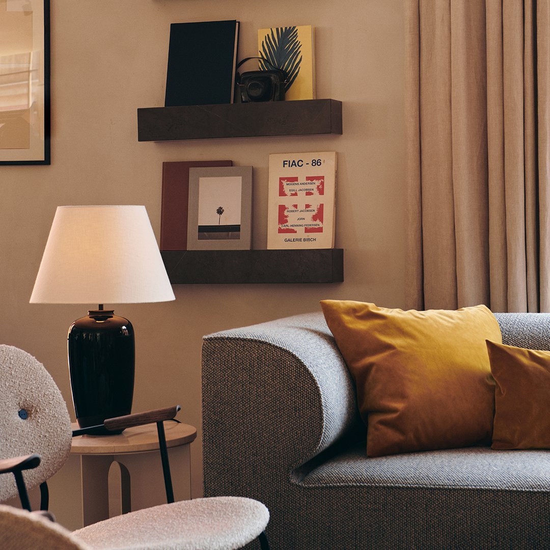 "Cozy gray sofa with mustard and brown accent pillows, soft beige curtains, and modern décor for a warm ambiance."