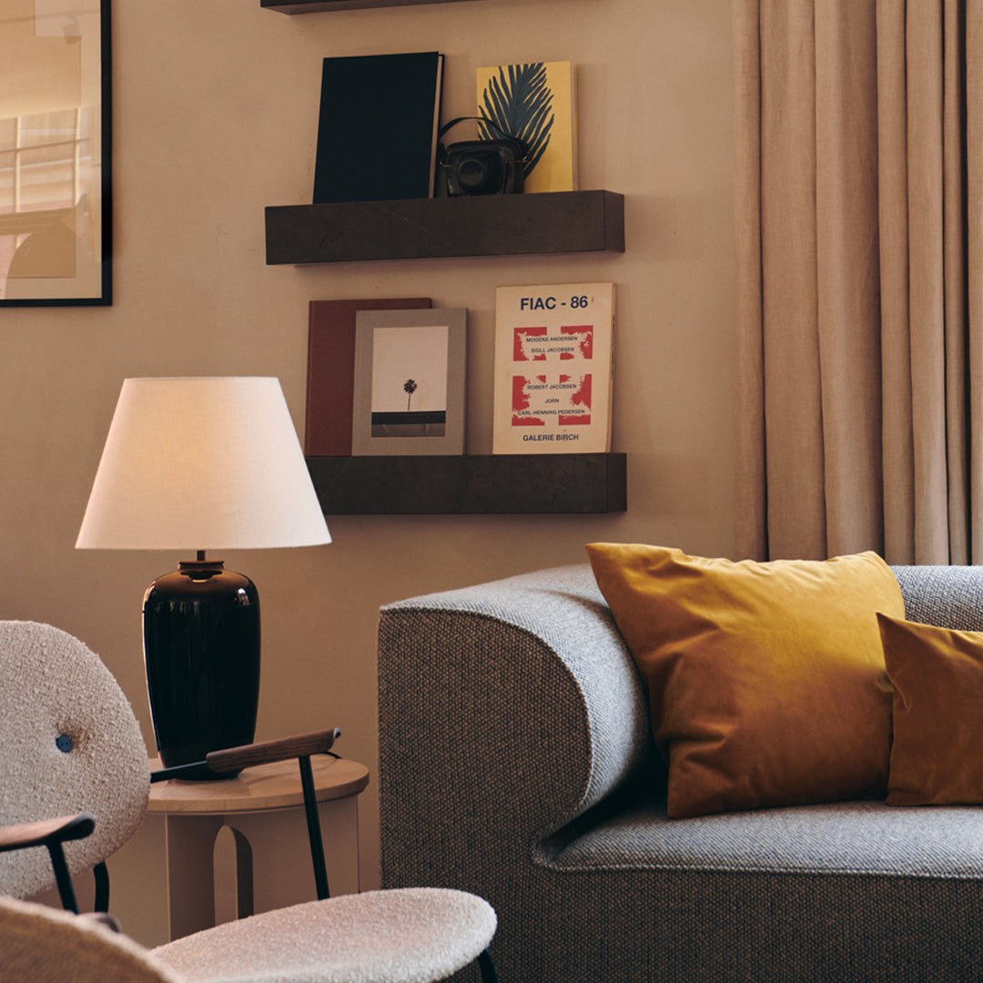 Elegant gray sofa with mustard yellow pillows, soft white lamp, and neutral-toned decor creating a cozy ambiance.