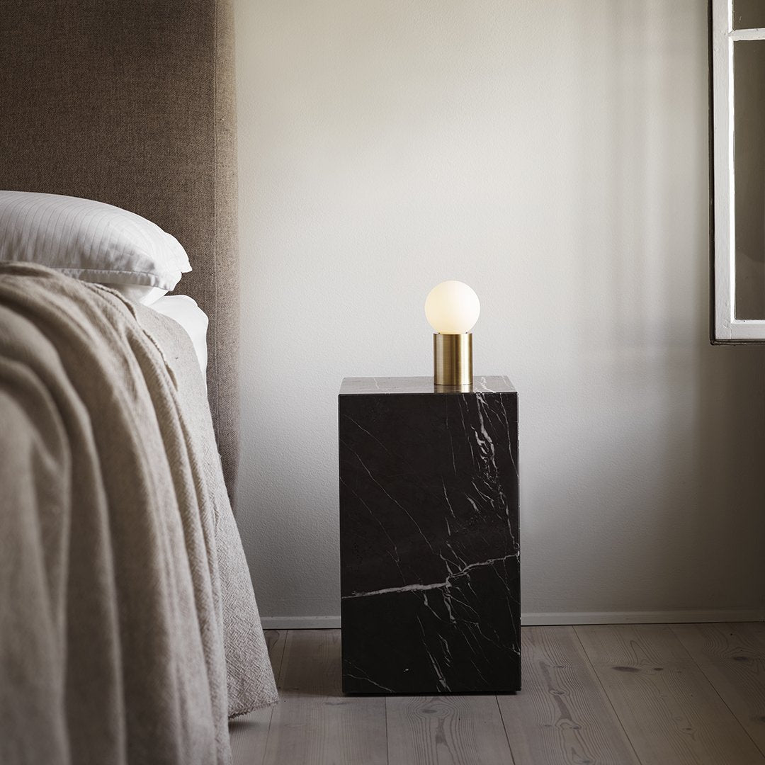 Black marble bedside table with white globe lamp and gold accent, featuring a sleek, modern design.