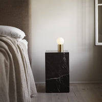 Black marble bedside table with white globe lamp and gold accent, featuring a sleek, modern design.