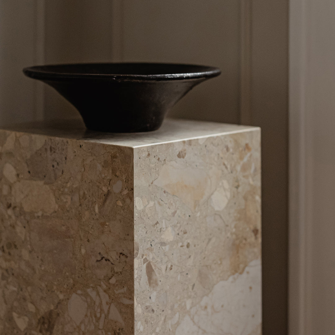 Black bowl on a light beige speckled stone pedestal, showcasing smooth textures and natural patterns.