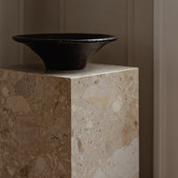 Black bowl on a light beige speckled stone pedestal, showcasing smooth textures and natural patterns.