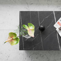 Black marble coffee table with white veining, featuring vibrant green and pink foliage in a clear vase.