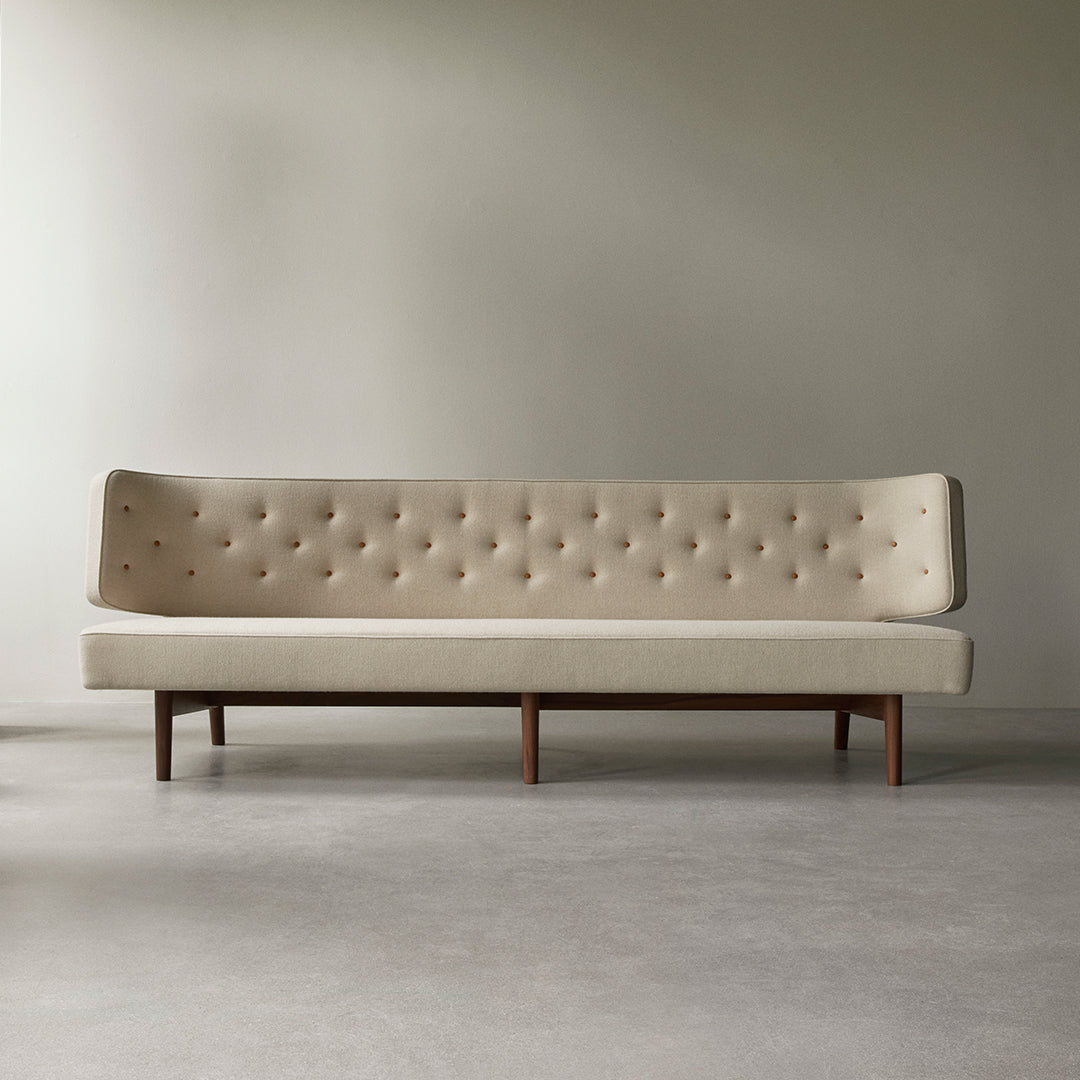 Beige tufted sofa with wooden legs against a neutral backdrop, featuring subtle buttons for added texture.