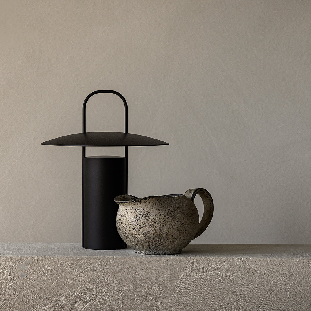 Black metal lantern and textured speckled beige ceramic pitcher on a neutral-toned surface. Elegant minimalist design.