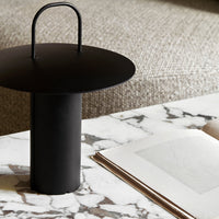 Black metal lamp with a round shade, minimalist design against a marble tabletop and textured beige background.
