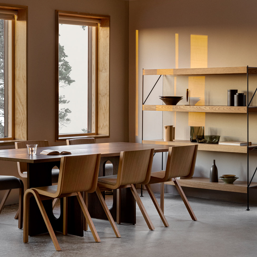 Modern dining room featuring warm wood tones, muted beige walls, and sleek black shelving with geometric lines.
