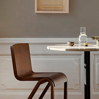 Brown wood chair with a sleek, curved design next to a round, light-colored table against a neutral gray backdrop.