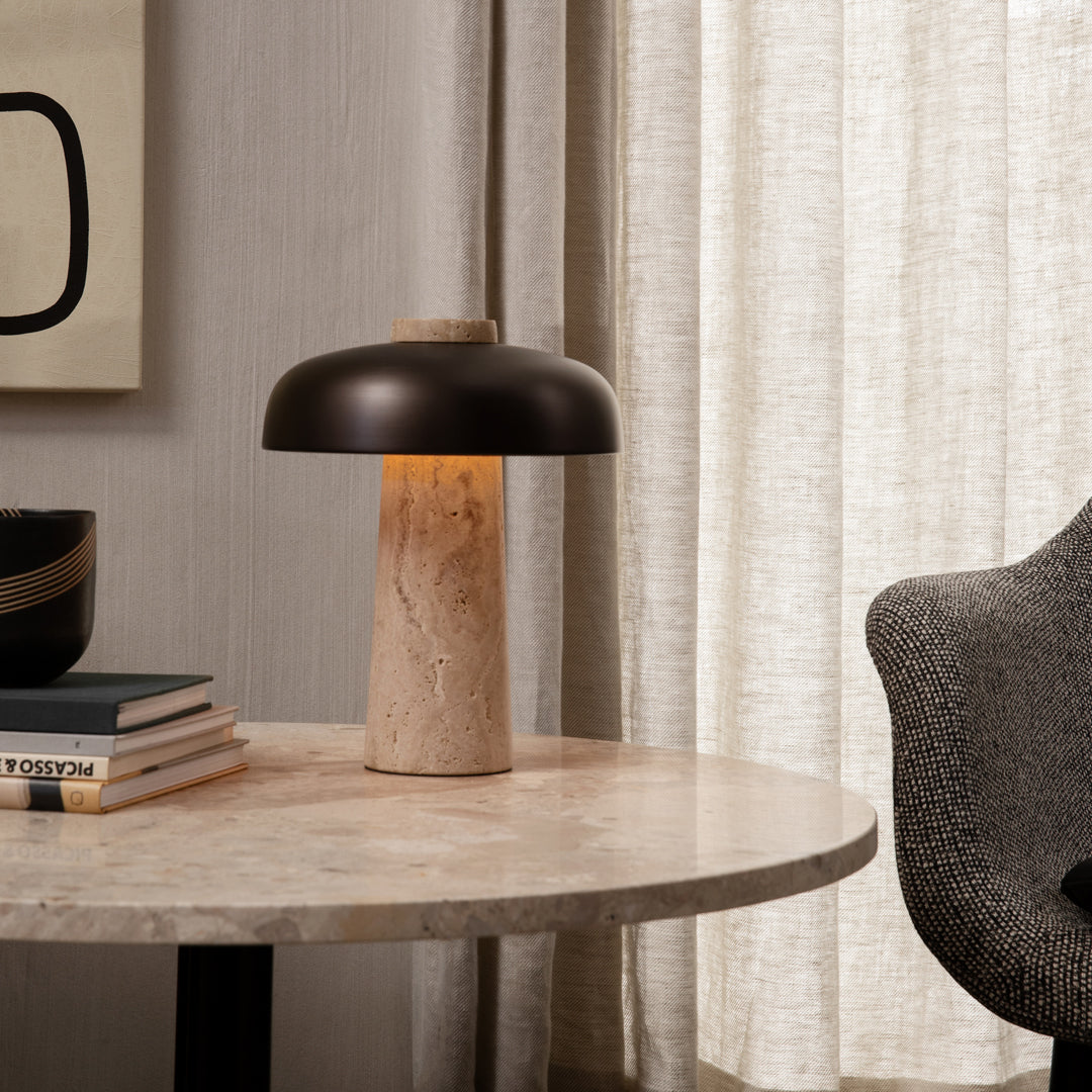 Modern table lamp with a dark bronze shade and a textured cream base, complemented by neutral fabrics and soft patterns.