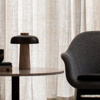 Modern gray chair with textured fabric, wooden lamp base, and neutral white curtains. Stylish and minimalistic design elements.
